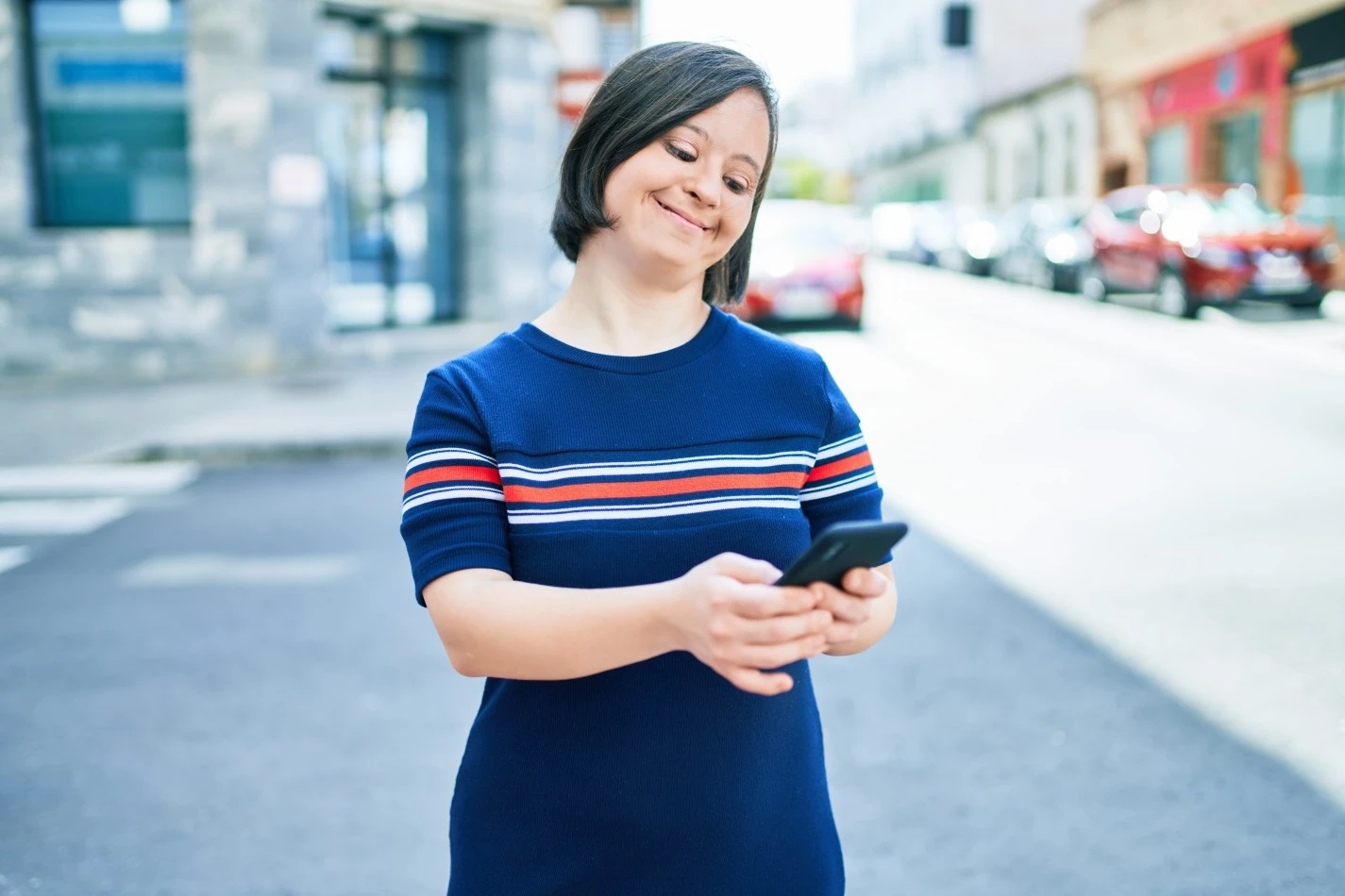 Woman with Down syndrome smiling while using a mobile phone